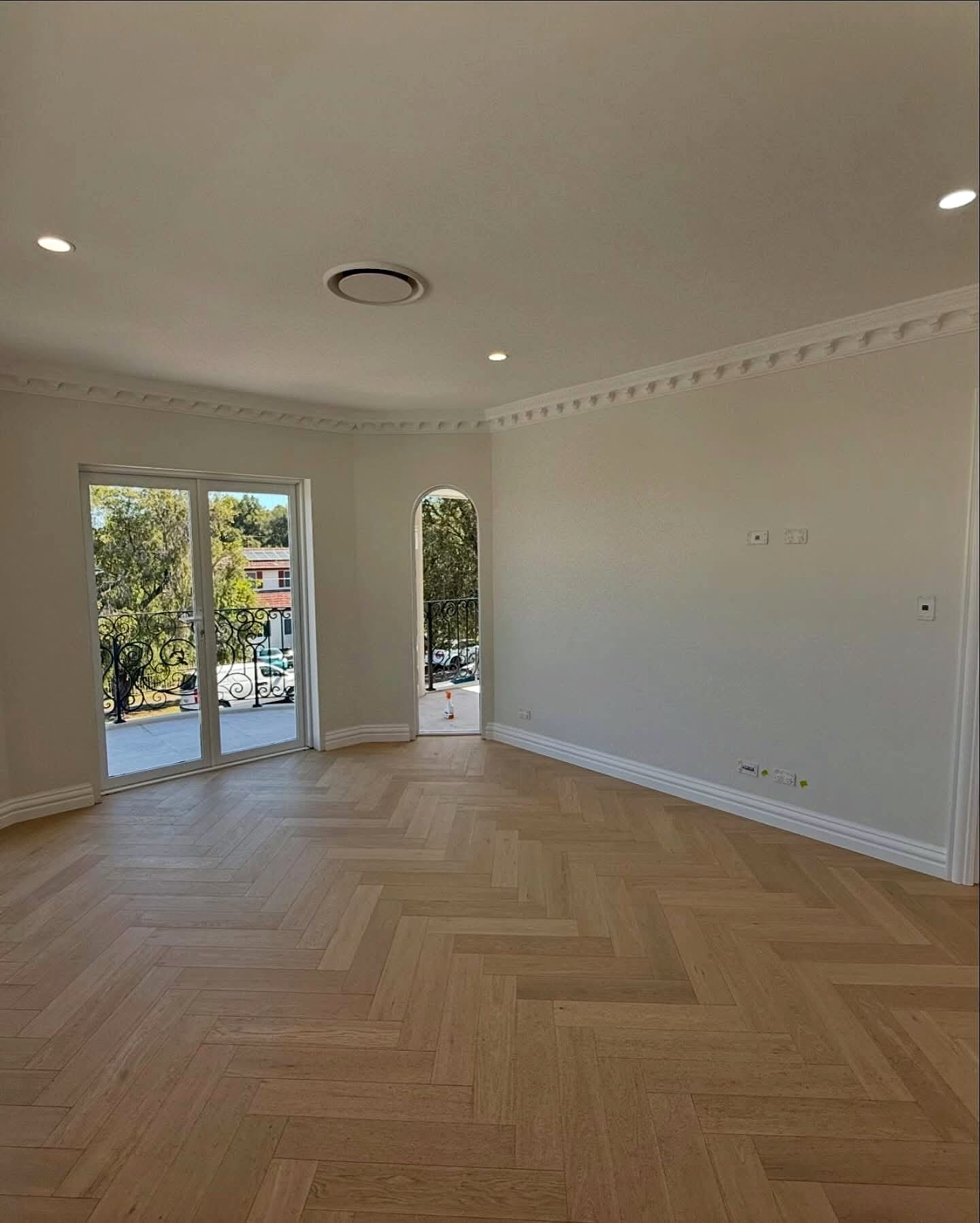 Empty room with a herringbone floor running to French doors, daylight across the boards
