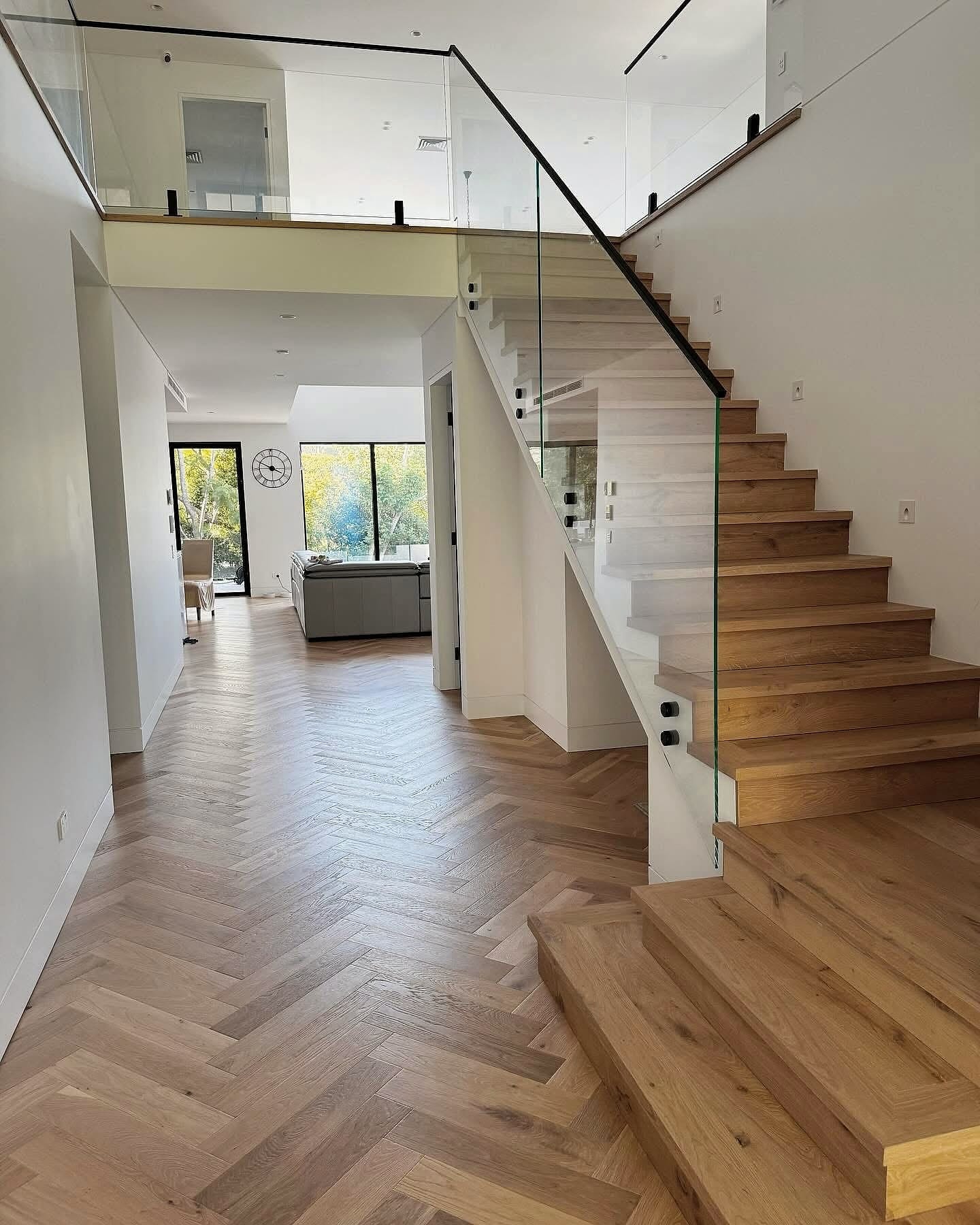 Herringbone hallway opening to a living area, timber stair with a glass balustrade to one side
