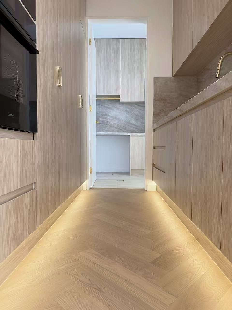 Hallway lined with timber joinery, concealed lighting washing down onto the floor
