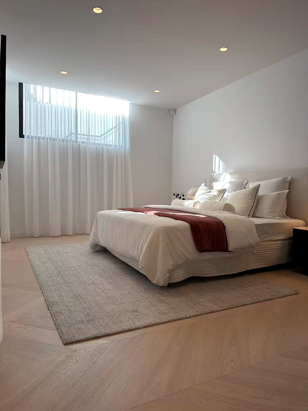 Bedroom with a large rug laid over a timber floor and sheer curtains at the window