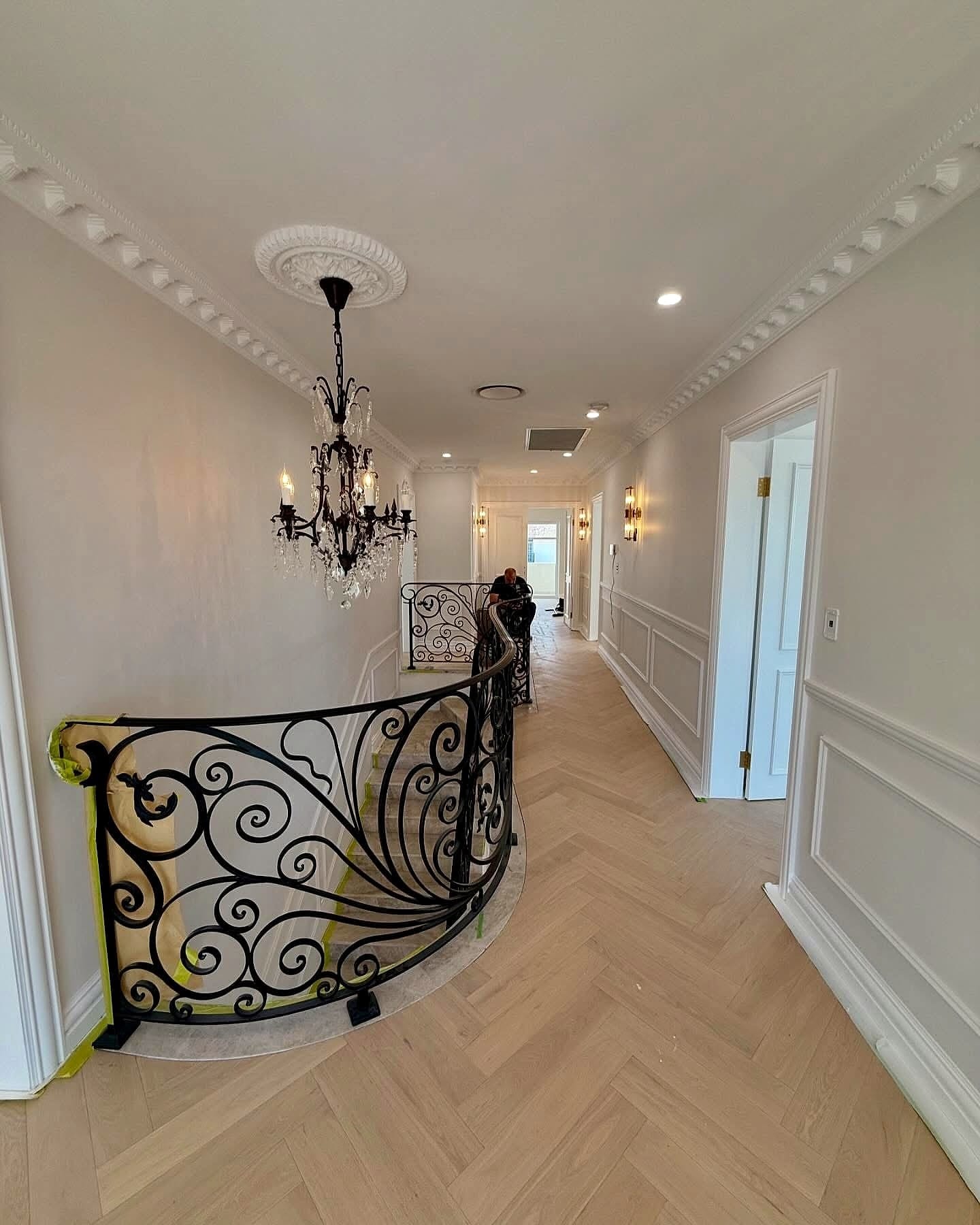Landing with an ornate wrought-iron balustrade and a chandelier above a herringbone floor
