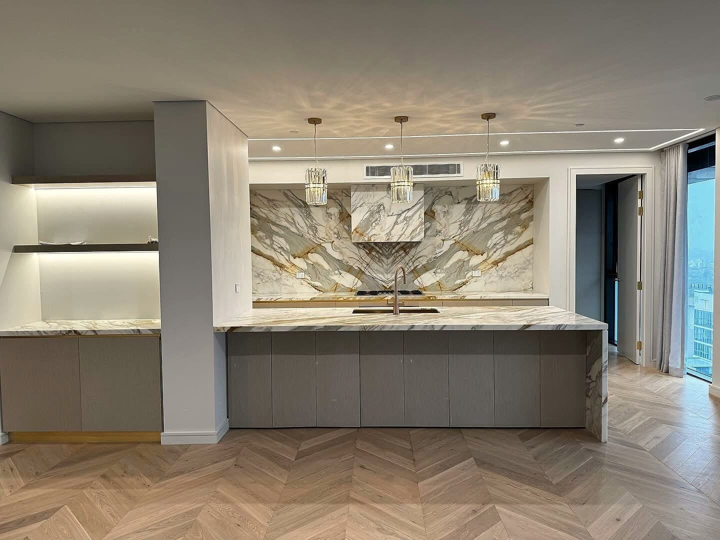 Chevron flooring beside a marble kitchen island under pendant lighting