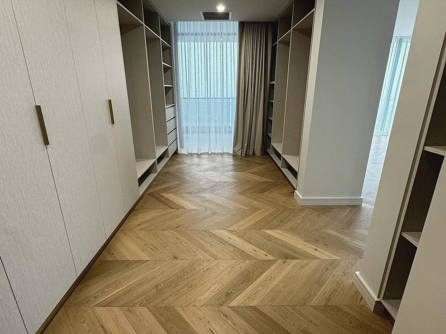 Walk-in wardrobe with chevron flooring and full-height joinery to a curtained window