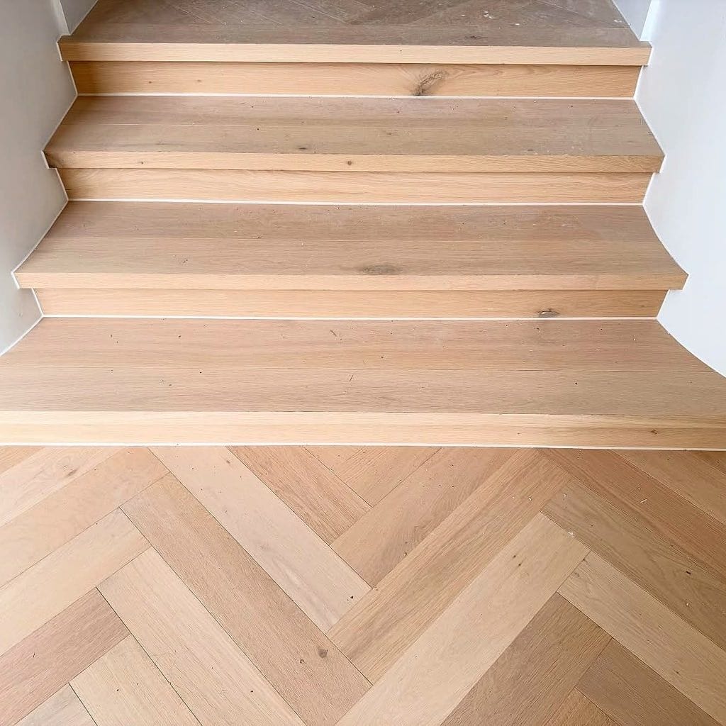 Herringbone boards meeting the base of a pale timber staircase
